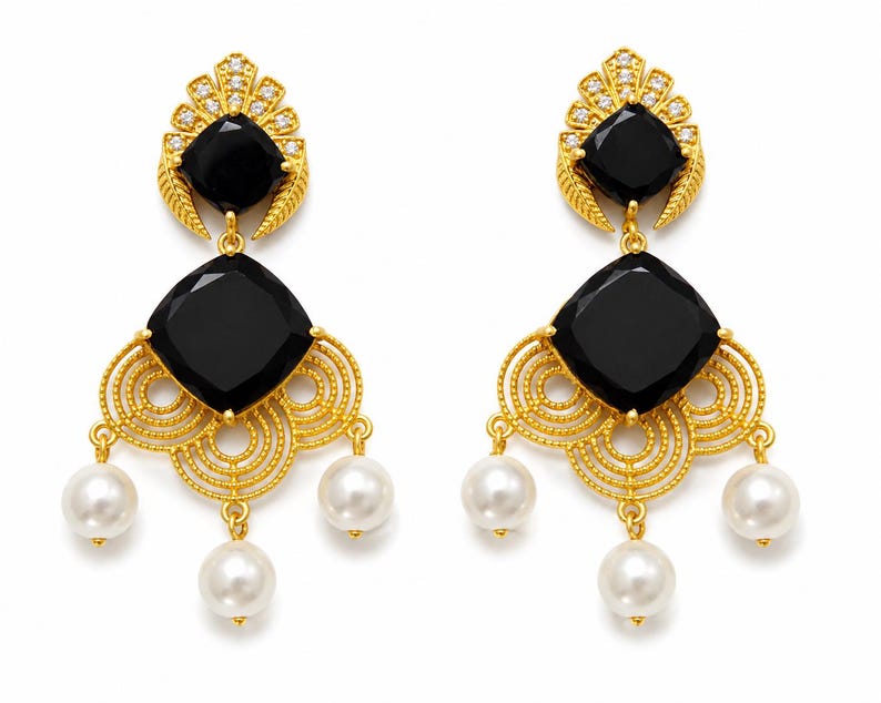 May include: A pair of gold-coloured chandelier earrings featuring black square-cut stones and white pearl drops. The earrings have a decorative filigree design and are adorned with small clear crystals.