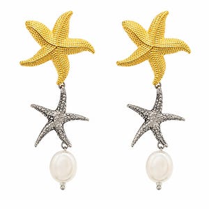 May include: A pair of drop earrings featuring a gold-toned starfish at the top, a silver-toned starfish suspended below, and a single white oval pearl dangling at the bottom. The starfish have a textured, granular surface detail throughout.