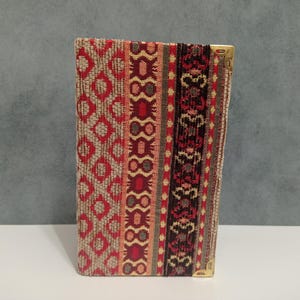 Puede incluir: Una cartera de tela con un diseño estampado en rojo, beige y negro, con esquinas de metal dorado.