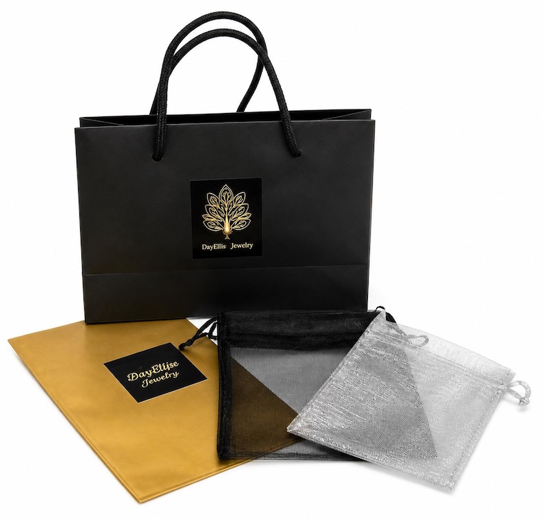 May include: A black shopping bag with a gold logo and black rope handles. The bag is next to a gold envelope, a black mesh bag, and a silver mesh bag. The logo on the bag and envelope reads "DayEllis Jewelry".
