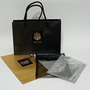 May include: A black gift bag with a gold logo and black handles, alongside a gold paper envelope and three small mesh bags. The logo on the bag reads "BeyBiju Jewelry".
