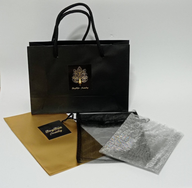 May include: A black gift bag with a gold logo and black handles, alongside a gold paper envelope and three small mesh bags. The logo on the bag reads "BeyBiju Jewelry".