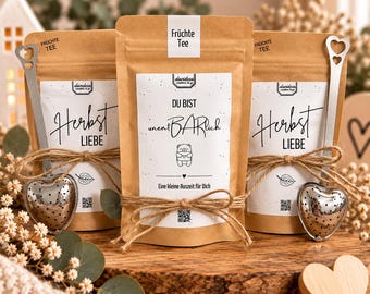 Könnte beinhalten: Drei braune Papiertüten mit Früchtetee und weißen Etiketten. Zwei Tüten sind mit Herbst Liebe beschriftet, eine mit DU BIST unentBARlich und einem Bären-Motiv. Zwei silberne herzförmige Tee-Eier sind mit einer Kordel an den Tüten befestigt.