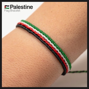 Może przedstawiać: Tkany bransoletka w kolorze czarnym, białym, czerwonym i zielonym z napisem "Palestine Flag Bracelet".