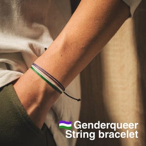 May include: A green, white, and purple string bracelet on a person's wrist. The bracelet is tied with a black string. The text "Genderqueer String bracelet" is below the image.