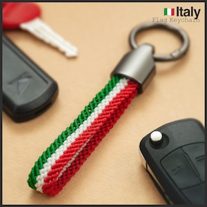 Pode incluir: Um porta-chaves com uma correia entrançada nas cores da bandeira italiana: verde, branco e vermelho. O porta-chaves tem um anel e uma tampa de metal prateado. O texto "Italy Flag Keychain" é visível.
