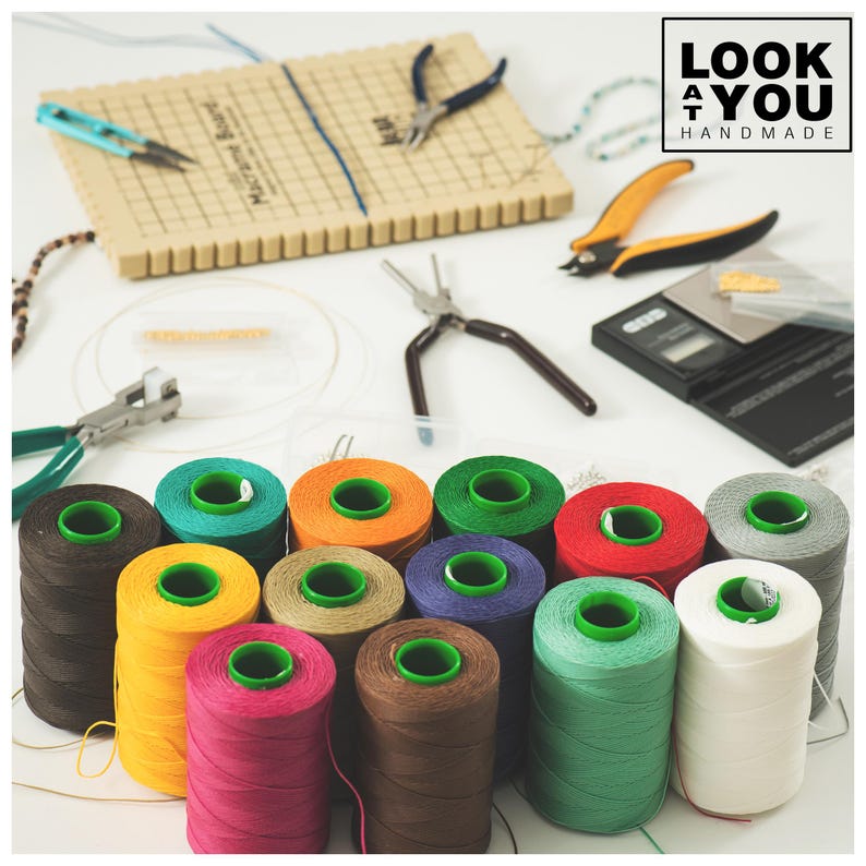 May include: A collection of colorful spools of thread, with various craft tools and a macrame board. The spools are in shades of brown, teal, orange, green, red, purple, yellow, pink, and white. Tools include pliers, scissors, and a small scale.