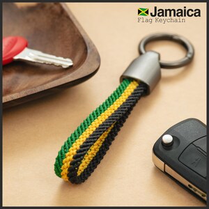 Könnte beinhalten: Ein Schlüsselanhänger mit den Farben der jamaikanischen Flagge: Grün, Gelb und Schwarz. Der Schlüsselanhänger hat einen geflochtenen Riemen und einen Metallring. Der Text "Jamaica Flag Keychain" ist sichtbar. Schlüssel und ein Autoschlüsselanhänger sind ebenfalls vorhanden.