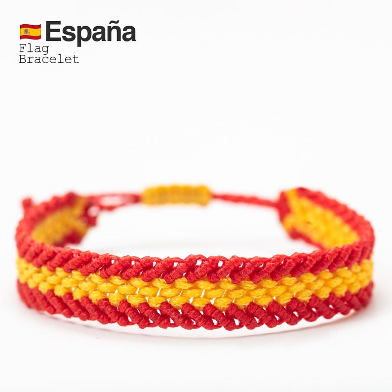 May include: A red and yellow woven bracelet, featuring the colors of the Spanish flag. The bracelet has a braided design with a red and yellow pattern. The text "Espa&ntilde;a" and "Flag Bracelet" are visible in the upper left corner.