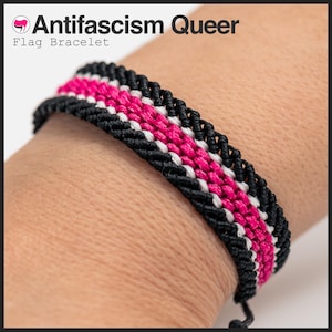 May include: A woven bracelet with a black, white, and pink flag design. The bracelet has the text "Antifascism Queer Flag Bracelet" in the upper left corner. The bracelet is made of woven threads.