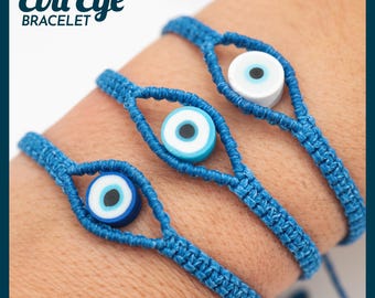 May include: Three blue Evil Eye bracelets are displayed, each featuring a woven design and a central eye-shaped bead. The beads have a white center with a blue and black outline. The bracelets are on a wrist.