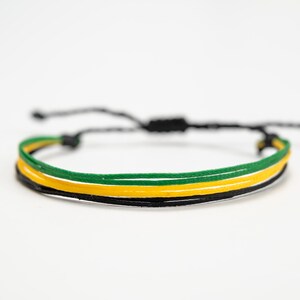 K&ouml;nnte beinhalten: Verstellbares Armband mit drei B&auml;ndern in Schwarz, Gelb und Gr&uuml;n. Es hat einen Schiebeknotenverschluss f&uuml;r eine individuelle Passform. Die Farben sind lebendig und das Design ist schlicht, f&uuml;r den Alltag geeignet.