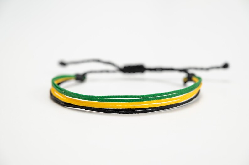 K&ouml;nnte beinhalten: Verstellbares Armband mit drei B&auml;ndern in Schwarz, Gelb und Gr&uuml;n. Es hat einen Schiebeknotenverschluss f&uuml;r eine individuelle Passform. Die Farben sind lebendig und das Design ist schlicht, f&uuml;r den Alltag geeignet.