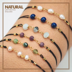 Op de afbeelding: Een set van zes armbanden met zwart koord en gouden accenten. Elke armband heeft een andere edelsteen, waaronder parels, lapis lazuli, aquamarijn, robijn, smaragd en peridoot. De armbanden zijn gelabeld met "NATURAL Gemstones Bracelet".