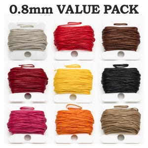 Könnte beinhalten: Eine Sammlung von neun Spulen mit 0,8 mm gewachster Kordel in verschiedenen Farben, darunter Rot, Braun, Gelb und Schwarz. Der Text "0,8 mm VALUE PACK" ist oben zu sehen. Jede Spule ist ordentlich auf einem weißen Kunststoffhalter aufgewickelt.