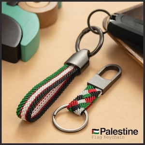 Puede incluir: Dos llaveros con correas tejidas con los colores de la bandera palestina: verde, blanco, negro y rojo. Un llavero tiene una correa larga y el otro una correa corta con un cierre metálico. El texto "Palestine Flag Keychain" es visible.