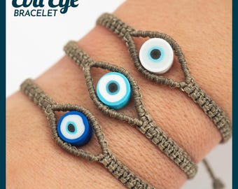 May include: Three macrame bracelets with evil eye beads. The bracelets are made of a tan-colored cord and feature blue, white, and blue evil eye beads. The text "Evil Eye Bracelet" is in the upper left corner.