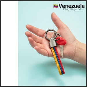 May include: A Venezuela flag keychain with a braided strap in yellow, blue, and red. The keychain is held in a hand, with a key attached. The text "Venezuela Flag Keychain" is visible.