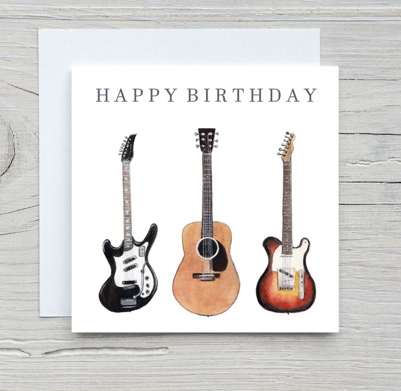 May include: A white greeting card with the words "HAPPY BIRTHDAY" above three watercolor guitars. The guitars are a black electric guitar, a brown acoustic guitar, and a red and yellow electric guitar.