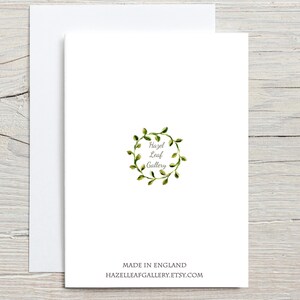 Peut inclure: Une carte de v&oelig;ux blanche avec une enveloppe assortie. La carte pr&eacute;sente une couronne de feuilles verte &agrave; l'aquarelle avec le texte "Hazel Leaf Gallery". En dessous, le texte indique "MADE IN ENGLAND" et "HAZELLEAFGALLERY.ETSY.COM."