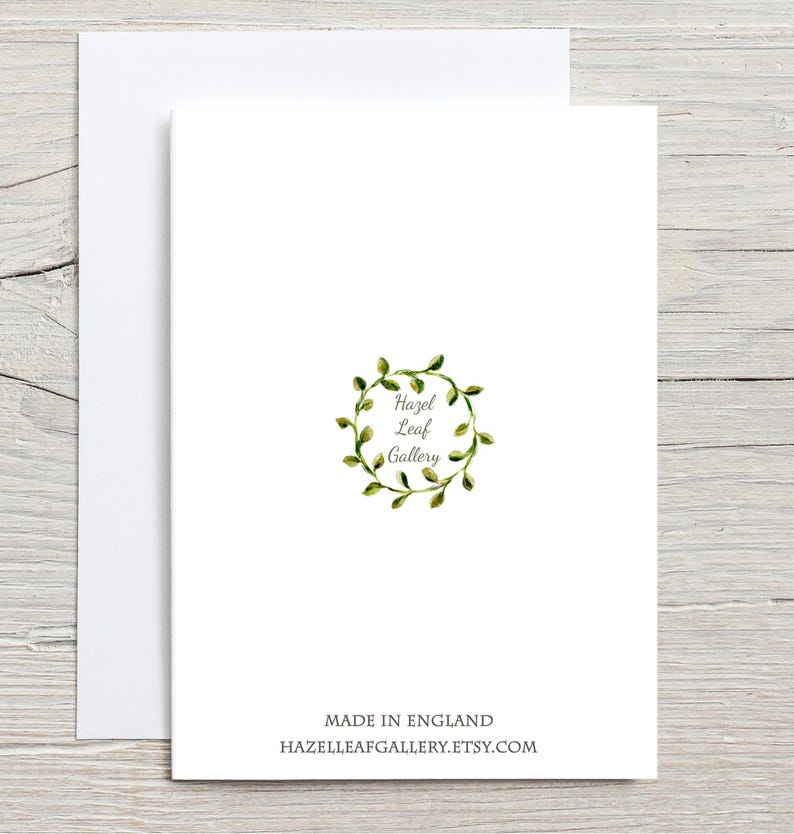 Peut inclure: Une carte de v&oelig;ux blanche avec une enveloppe assortie. La carte pr&eacute;sente une couronne de feuilles verte &agrave; l'aquarelle avec le texte "Hazel Leaf Gallery". En dessous, le texte indique "MADE IN ENGLAND" et "HAZELLEAFGALLERY.ETSY.COM."