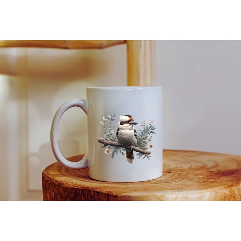 May include: White ceramic mug featuring a colourful illustration of a kookaburra bird perched on a branch with green leaves and white flowers.