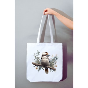 May include: White canvas tote bag featuring a colourful illustration of a kookaburra bird perched on a branch with green leaves and flowers.