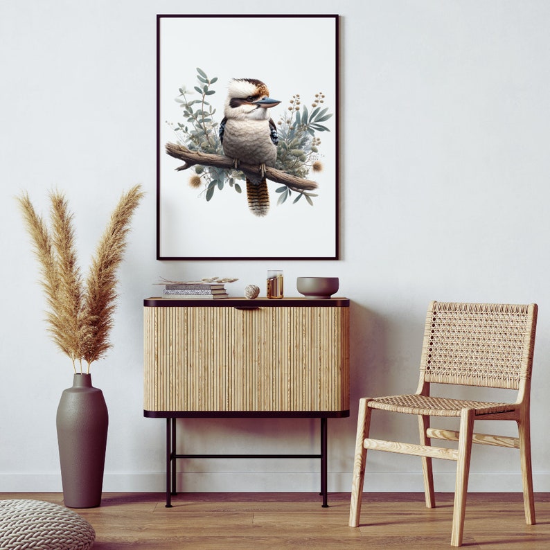May include: A framed print of a kookaburra bird perched on a branch with green leaves and flowers. The print is hanging on a white wall above a wooden cabinet with a woven rattan front.