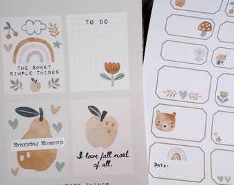 Pode incluir: Adesivos imprimíveis com ilustrações de um arco-íris, uma pêra, uma maçã, uma flor e um urso. Os adesivos são etiquetados com frases como "The Sweet Simple Things", "Everyday Moments" e "I love fall most of all".