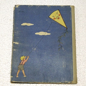 May include: A vintage children's book cover with a blue background and a child flying a kite. The kite is yellow with a smiling face and red cheeks. The text on the cover reads "23 июл."
