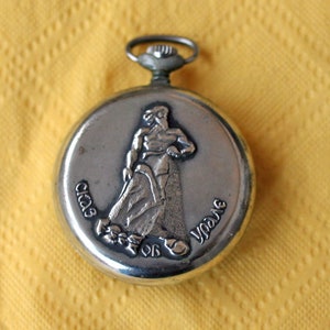 May include: Silver pocket watch with a raised image of a person holding a rope. The watch face reads "Club de Yo-Yo".
