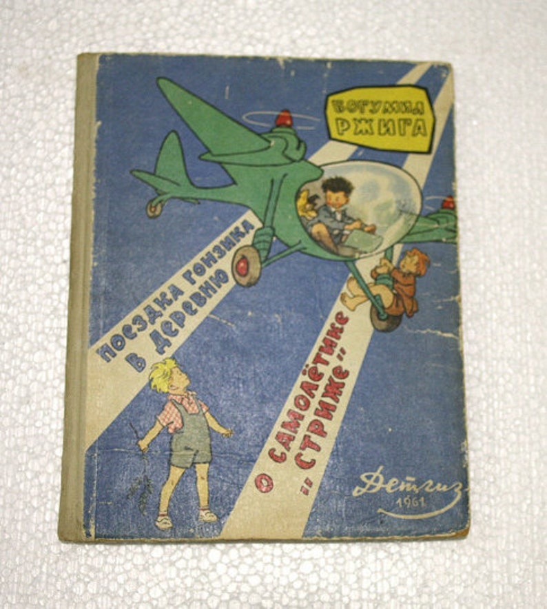 May include: A vintage children's book cover with a blue, green, and yellow illustration of a plane with a bubble canopy. The text on the cover reads "Посадка гонщика в деревню" and "О самолётчике "стрижке"..."  The book is titled "Вот уж книга".