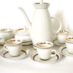 May include: A white porcelain tea set with gold trim. The set includes a teapot, sugar bowl, creamer, and six cups and saucers.