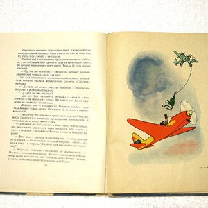 May include: An open book with a red and yellow airplane illustration on the right page. The left page has text in Russian. The book is on a white surface.