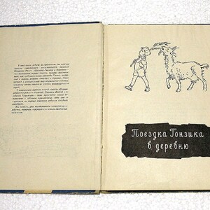 May include: An open book with a black and white illustration of a boy walking a goat. The text on the page reads "Поездка Тонзика в деревню" which translates to "Tonzik's Trip to the Village".