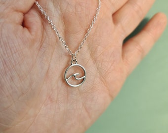 May include: A silver chain necklace with a small, circular pendant featuring a wave design.
