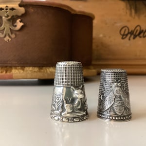 Puede incluir: Dos dedal de plata con diseños intrincados. Un dedal presenta un ciervo y motivos florales, mientras que el otro tiene un diseño de abeja.