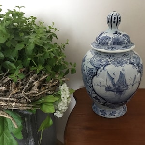 Op de afbeelding: Een blauwe en witte keramische pot met deksel, met een traditioneel Nederlands ontwerp van een zeilboot en bloemmotieven.