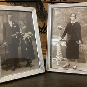 Puede incluir: Dos marcos de fotos plateados con fotografías en blanco y negro de una pareja y una mujer. La pareja está vestida con atuendos formales y la mujer lleva un vestido oscuro.