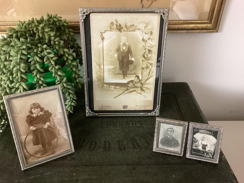 May include: Three silver-toned picture frames with black and white photos. The top frame features a man in a suit and hat. The left frame features a young girl holding a hoop. The right frame features a man in a suit and tie.