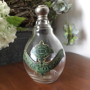 May include: A clear glass bottle with a silver stopper and a green label that reads "Eau de Cologne Blue & Gold Double".