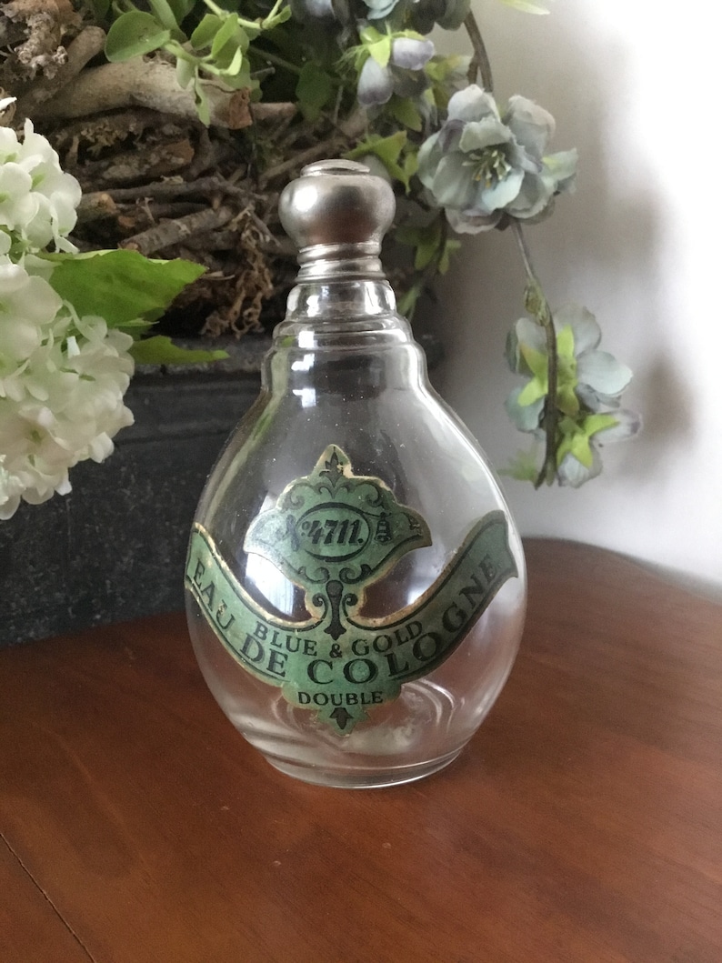 May include: A clear glass bottle with a silver stopper and a green label that reads "Eau de Cologne Blue & Gold Double".