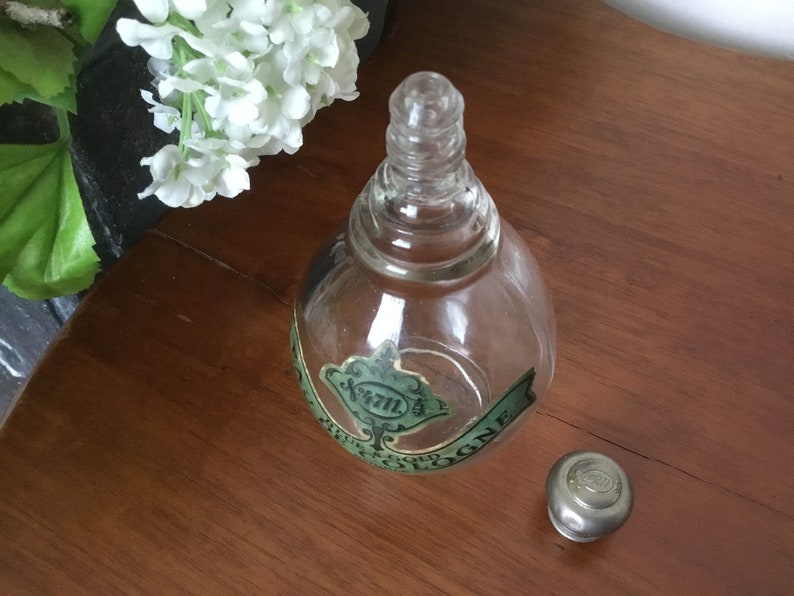 May include: A clear glass bottle with a green label that reads "4711" and "EAU DE COLOGNE". The bottle has a silver cap.