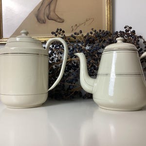 Puede incluir: Dos teteras de cerámica blanca con ribetes dorados. Las teteras tienen un diseño clásico y son perfectas para servir té.