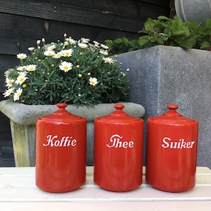 Puede incluir: Tres botes de cerámica roja con tapas blancas y letras blancas. Los botes están etiquetados con "Koffie", "Thee" y "Suiker".