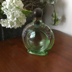 May include: A vintage green glass bottle with a dark brown stopper. The bottle has a circular design with a floral pattern and the words "English Lavender" printed on it.