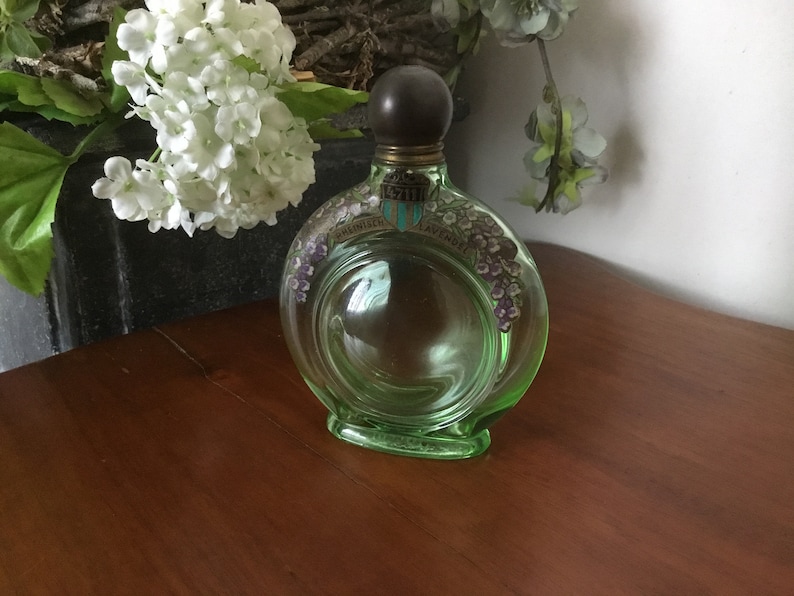 May include: A vintage green glass bottle with a dark brown stopper. The bottle has a circular design with a floral pattern and the words "English Lavender" printed on it.