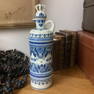 May include: A blue and white ceramic bottle with a lid and a spout. The bottle is decorated with a traditional Dutch design.