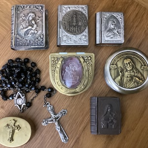 May include: A collection of religious items including a rosary with black beads, a silver and gold cross, a silver locket with a religious image, and several small silver and gold boxes with religious images.