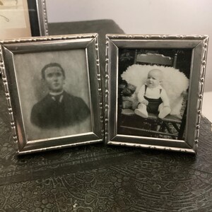 May include: Two silver picture frames with black and white photos. The left frame shows a man in a suit and tie. The right frame shows a baby sitting in a chair.